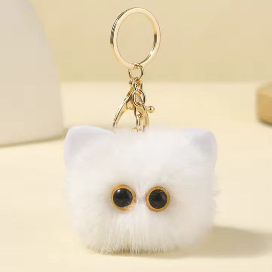 White fluffy keychain with black eyes on a light yellow background
