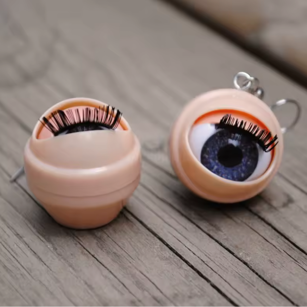 Eyeball-shaped blinking earrings with false eyelashes on a wooden surface