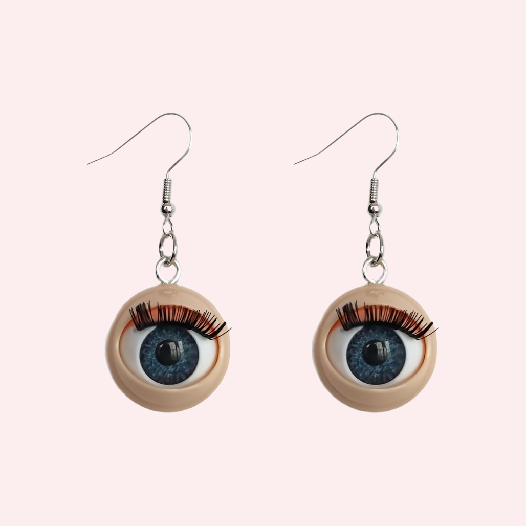 Eyeball-shaped earrings with blue irises and long lashes on a light pink background