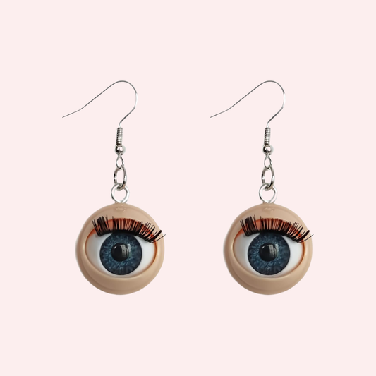 Eyeball-shaped earrings with blue irises and long lashes on a light pink background