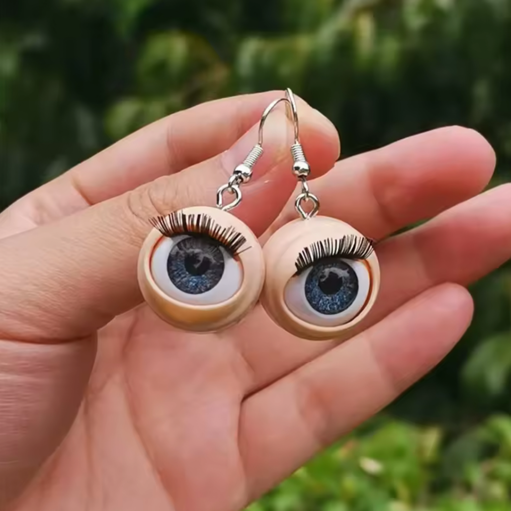 Eyeball-shaped earrings held in a hand with a blurred green background