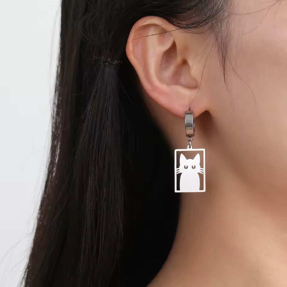 Silver earrings shaped like a rectangle with a silhouette of a cat where the eyes and whiskers are cut out